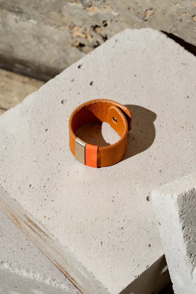 The Combo armband in cognac leder met afneembare contrastkleuren in oranje en goud. De armband sluit met een geweerknoop.