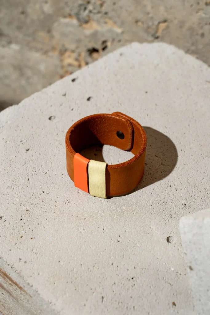 The Combo armband in cognac leder met afneembare contrastkleuren in oranje en lichtgeel. De armband sluit met een geweerknoop.