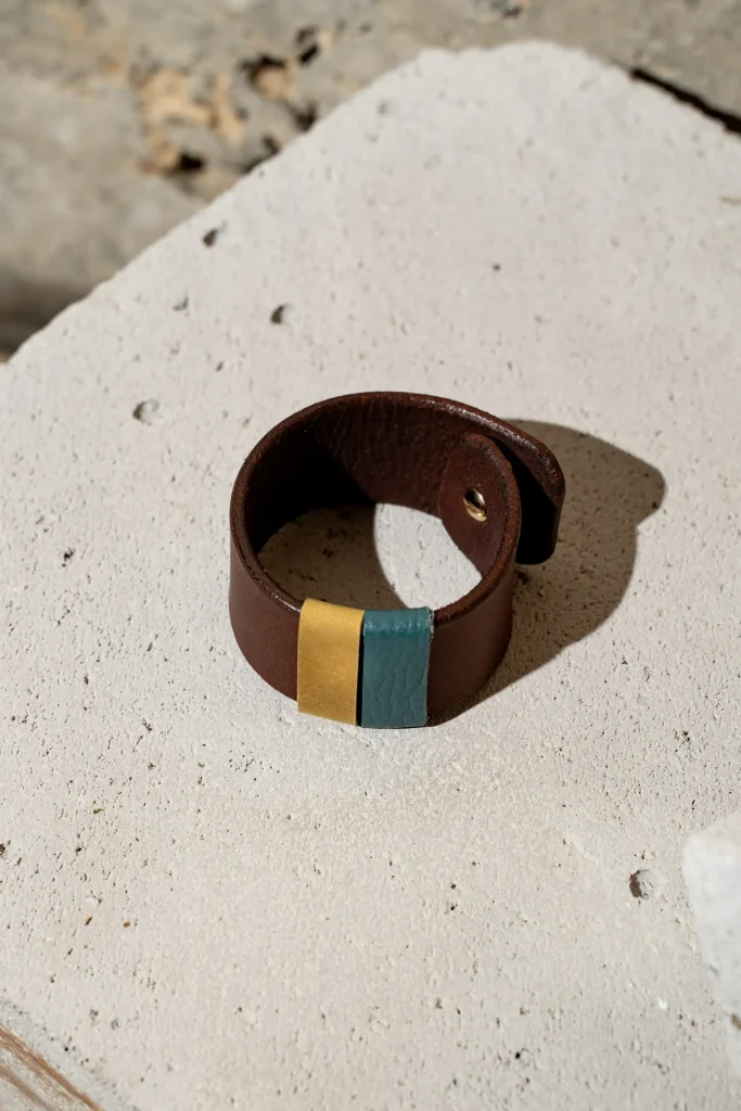 The Combo armband in donkerbruin leder met afneembare contrastkleuren in mosterd en jeansblauw. De armband sluit met een geweerknoop.