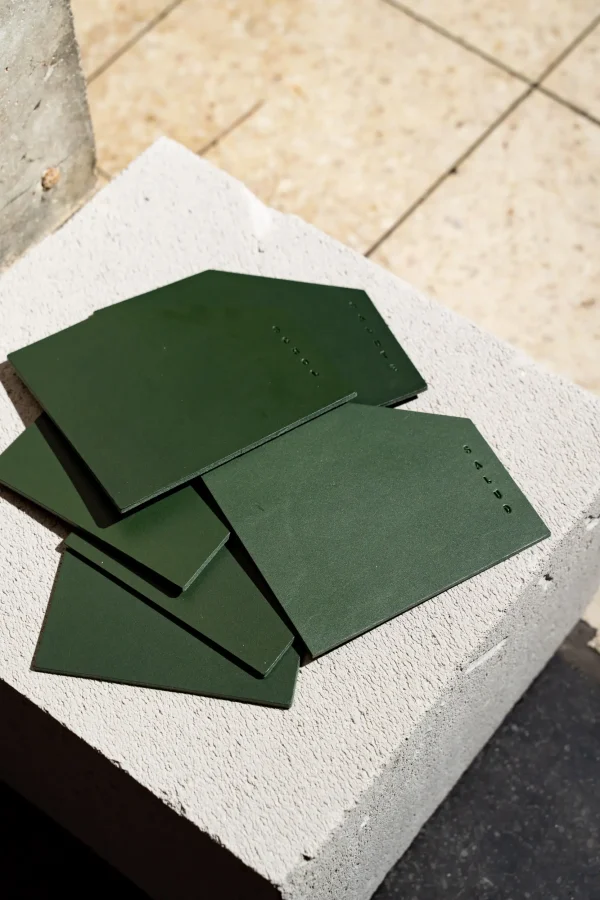 Set van 6 asymmetrische groene lederen coasters met in 6 talen 'schol' op.